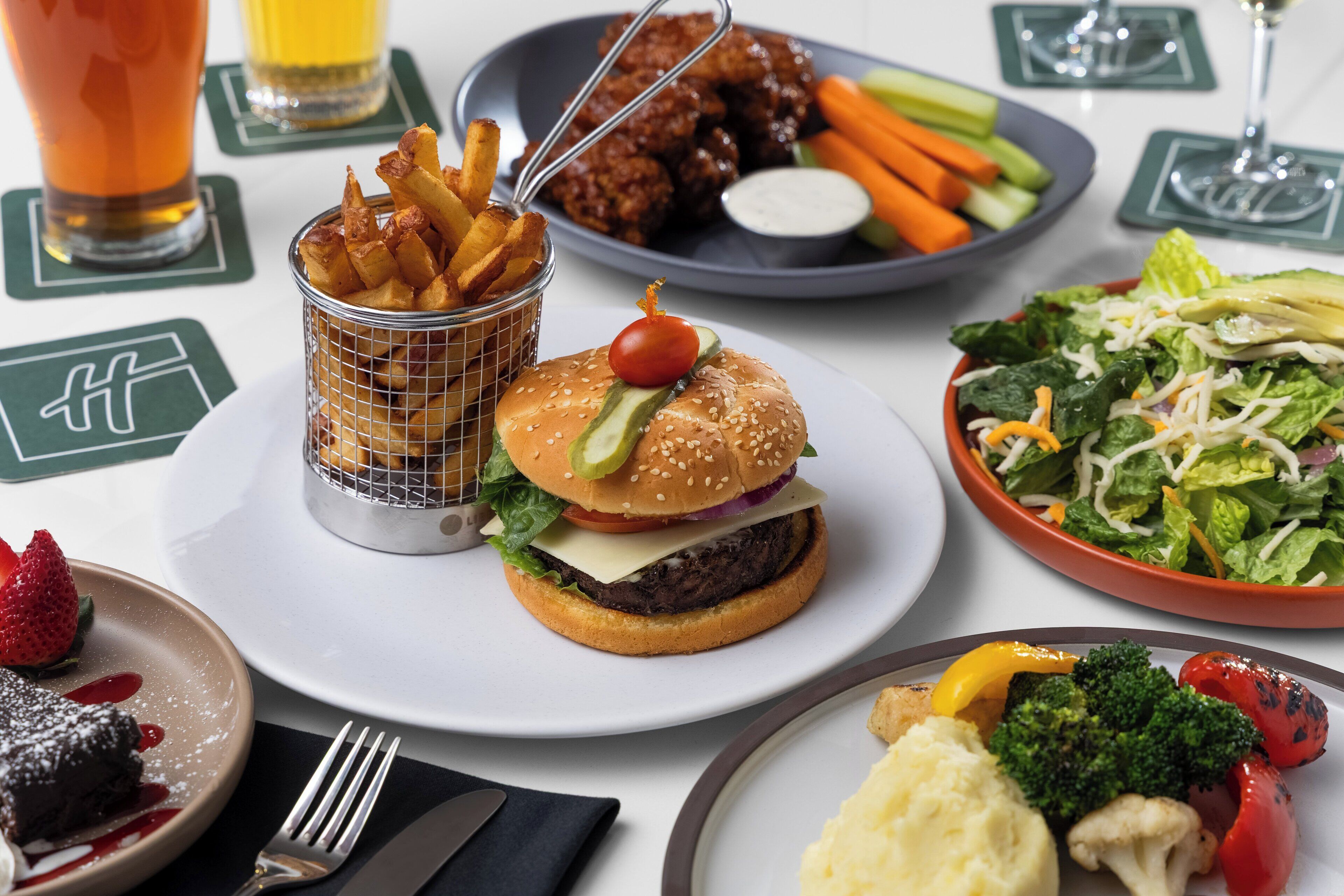 Una mesa con varios platos, incluyendo una hamburguesa, papas fritas, ensalada y un postre.