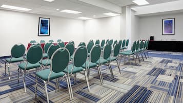 A conference room with rows of green chairs, a patterned carpet, and two framed abstract paintings on the walls.