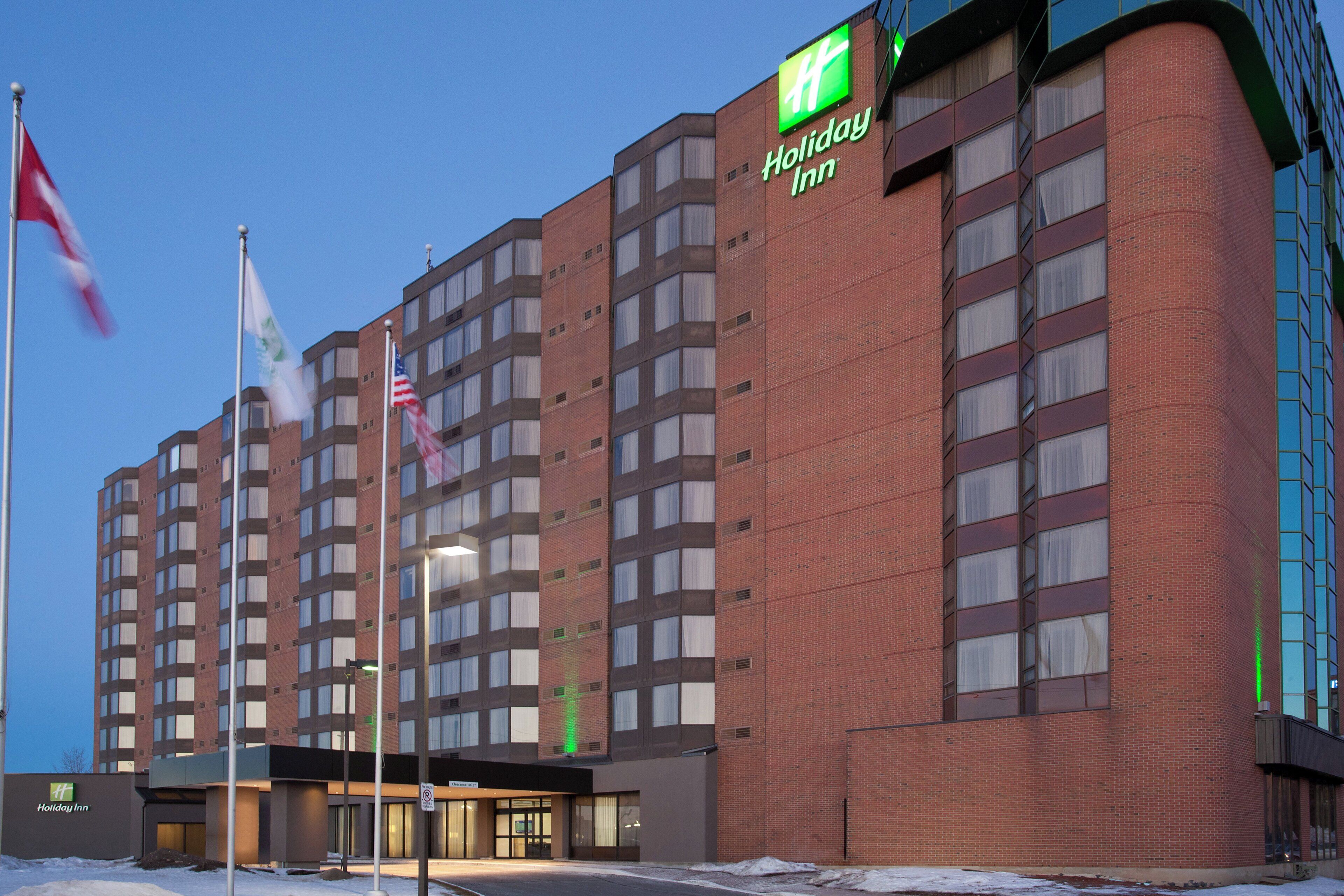 Un hotel Holiday Inn con fachada de ladrillo, múltiples ventanas y un cartel que indica la existencia de un estacionamiento.