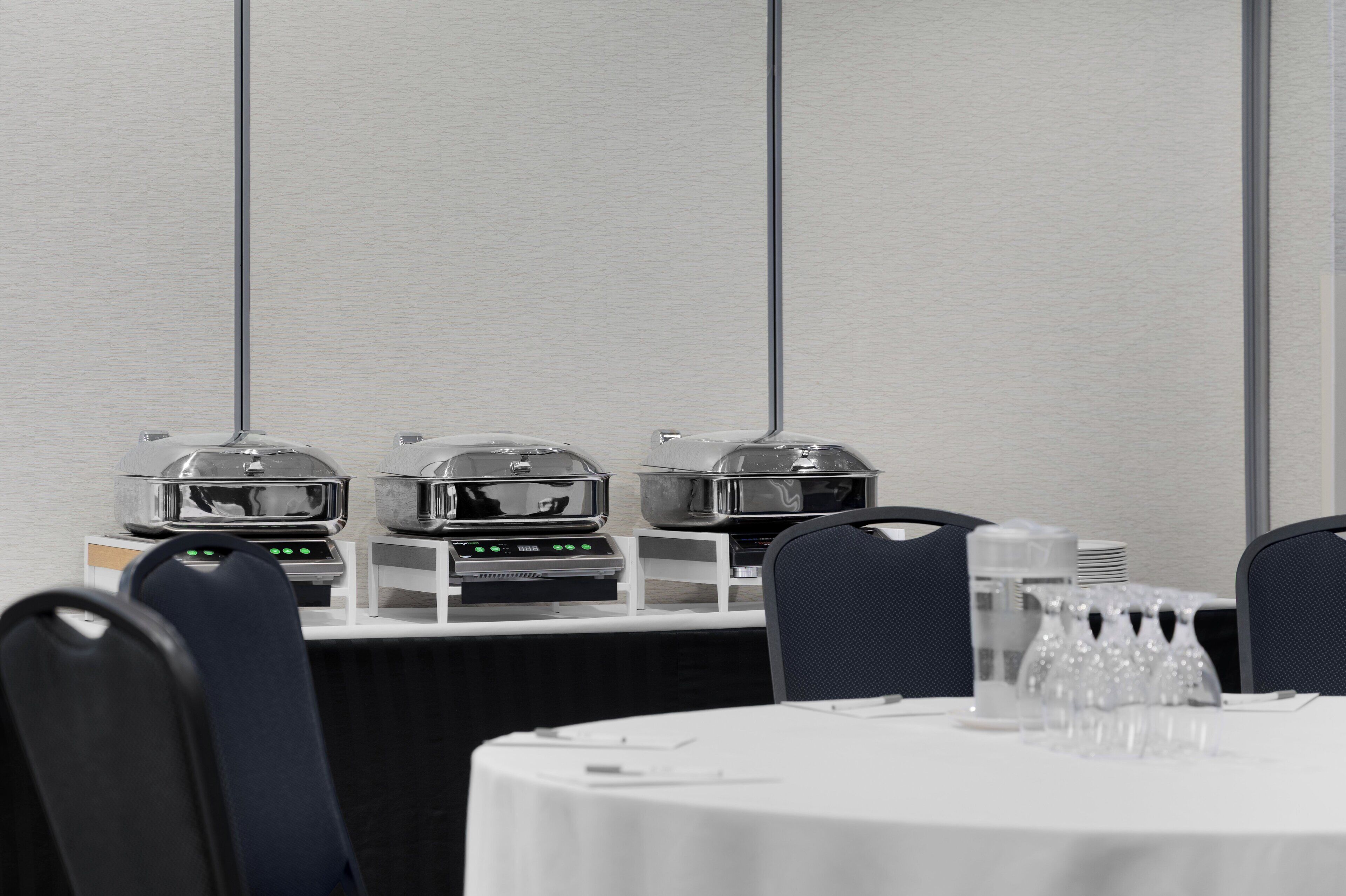 A conference room with a white table, chairs, and buffet stations with food warmers.