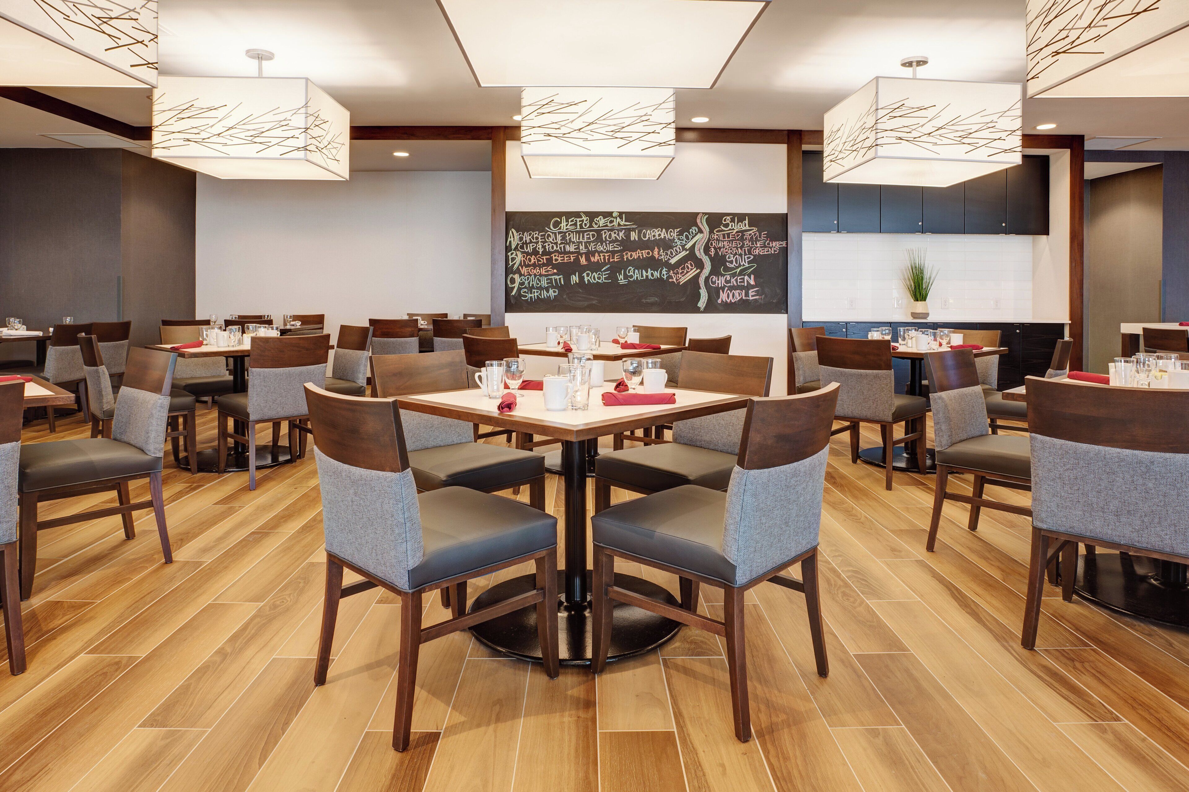 A restaurant with multiple tables and chairs, a chalkboard menu, and pendant lighting.