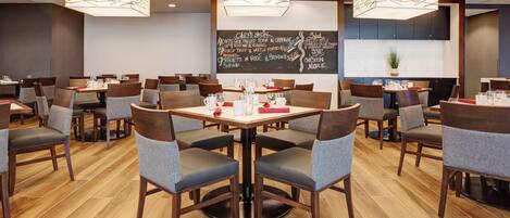 A restaurant with multiple tables and chairs, a chalkboard menu, and pendant lighting.