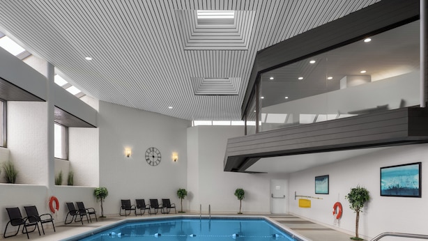 Una piscina interior moderna con un diseño geométrico en el techo, sillas de descanso y servicios integrados en la pared.