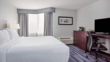 Habitación de hotel con una cama grande, un escritorio con computadora, una silla, unidad de aire acondicionado y un cuadro en la pared.