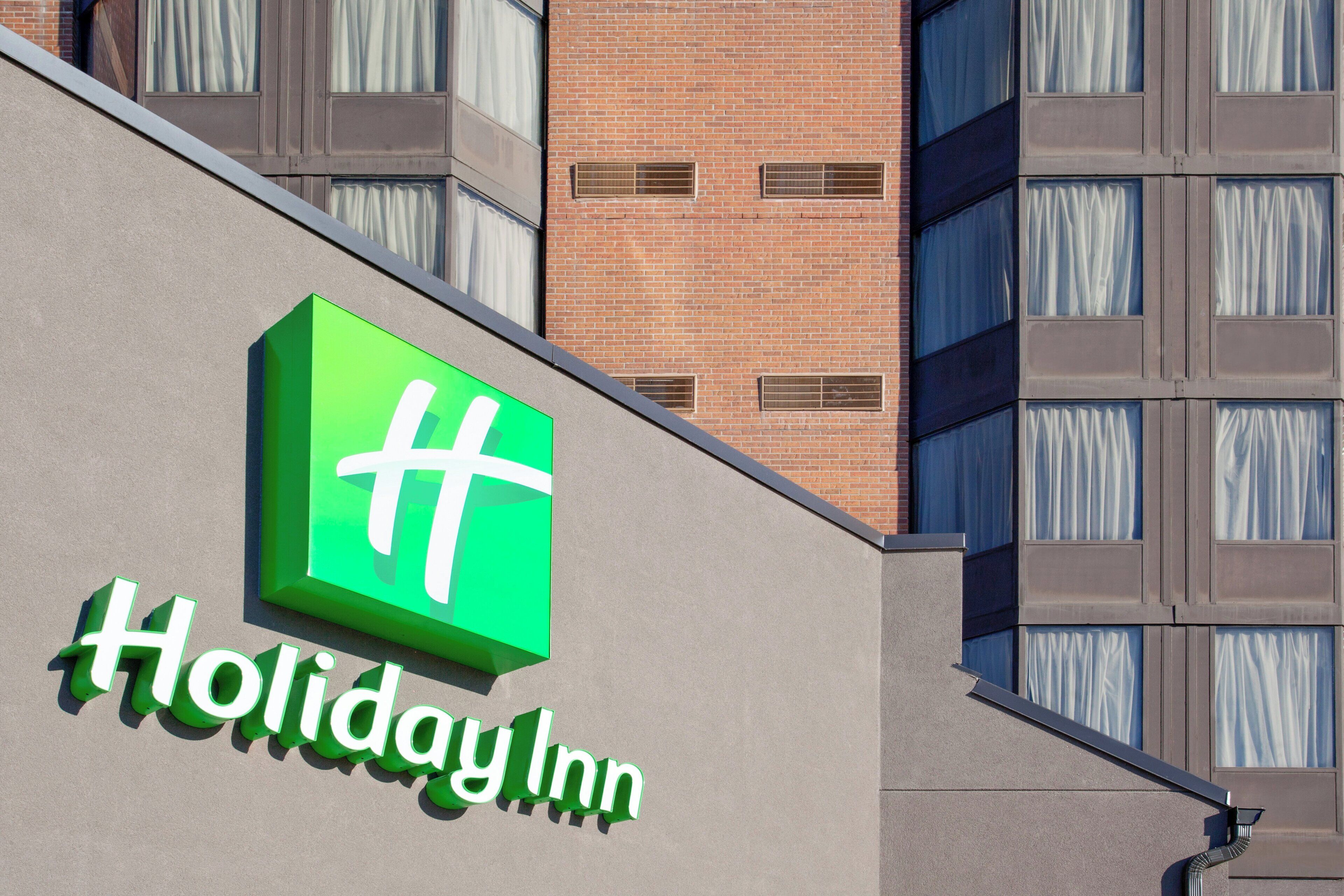 A Holiday Inn sign on a building facade with a brick wall and multiple windows.