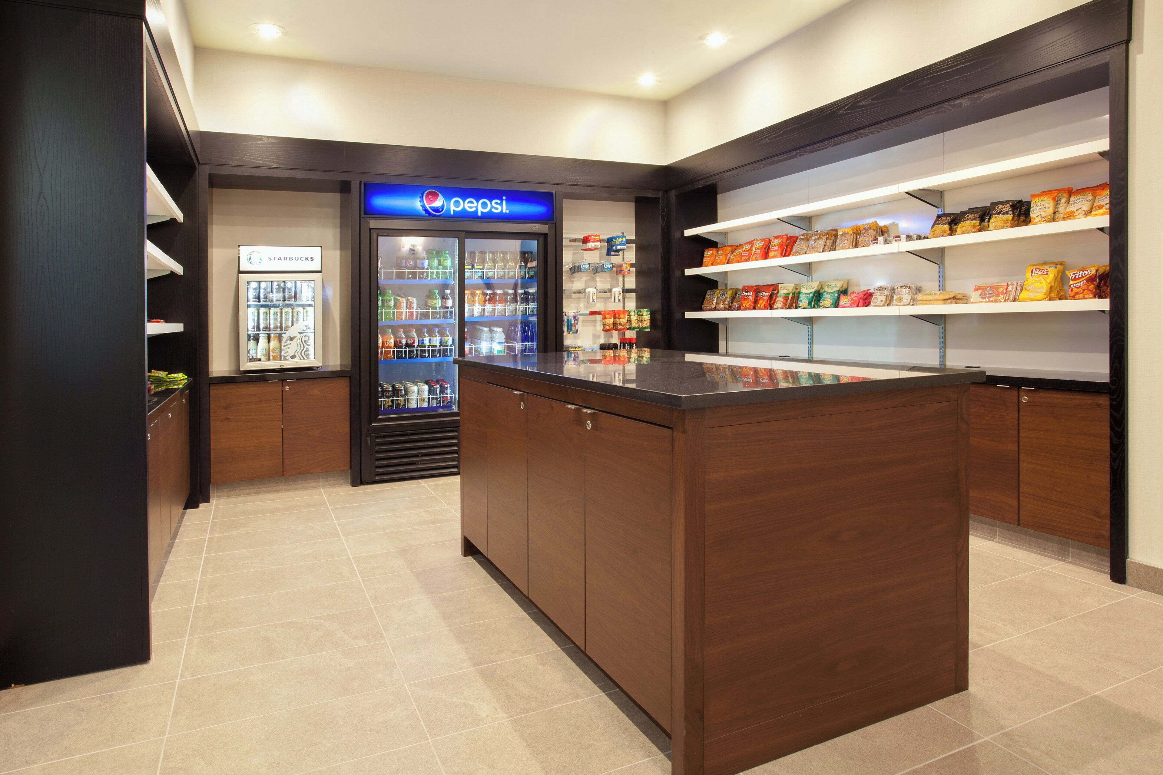 A clean, modern food service area with a Pepsi refrigerator, a Starbucks cooler, and shelves stocked with snacks.
