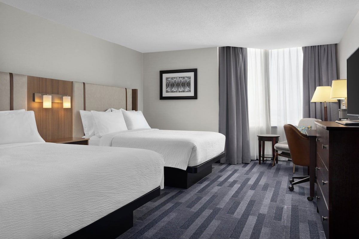 A hotel room with two beds, a desk, a chair, a TV, and a framed picture on the wall.
