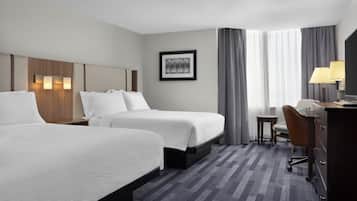 A hotel room with two beds, a desk, a chair, a TV, and a framed picture on the wall.