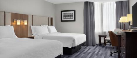 A hotel room with two beds, a desk, a chair, a TV, and a framed picture on the wall.