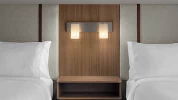 A hotel room with two beds, a wooden headboard, and a shelf with lights.