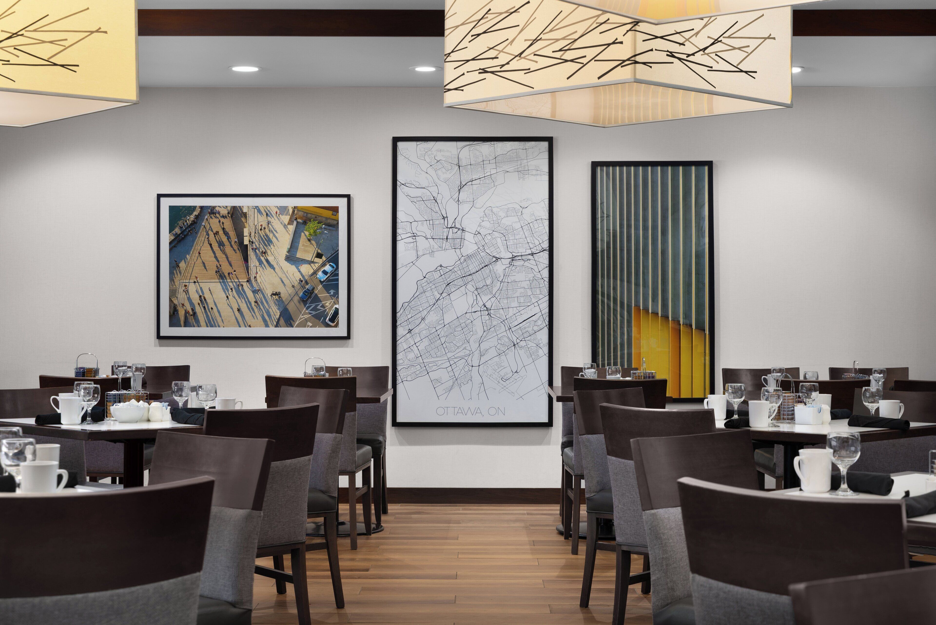 Een eetruimte met gedekte tafels, een grote kaart van Ottawa aan de muur en moderne verlichtingsarmaturen.
