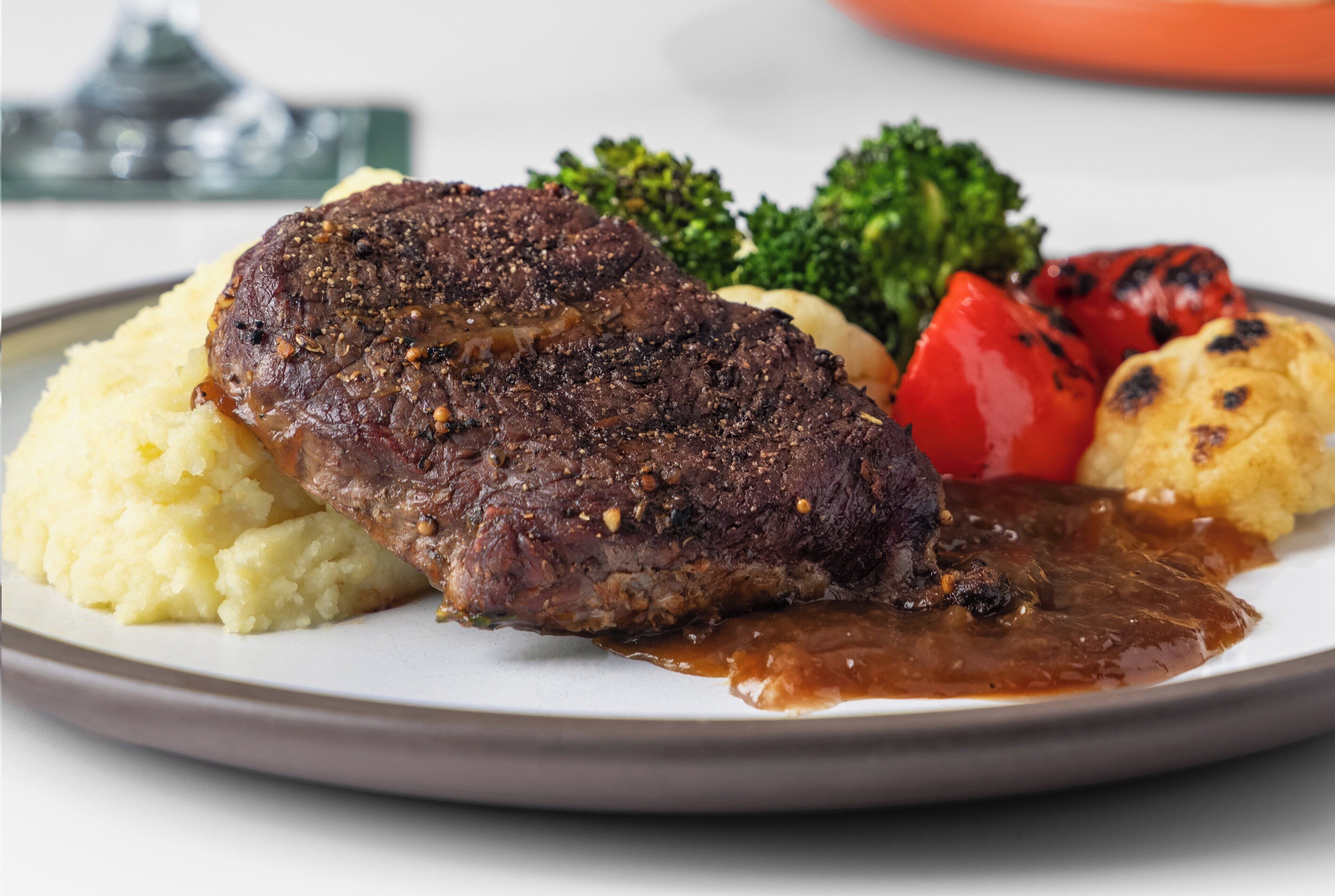 A plate with a steak, mashed potatoes, broccoli, and grilled vegetables.