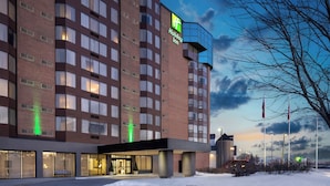 Un hotel Holiday Inn con fachada de ladrillo, ventanas grandes y un letrero iluminado en verde.