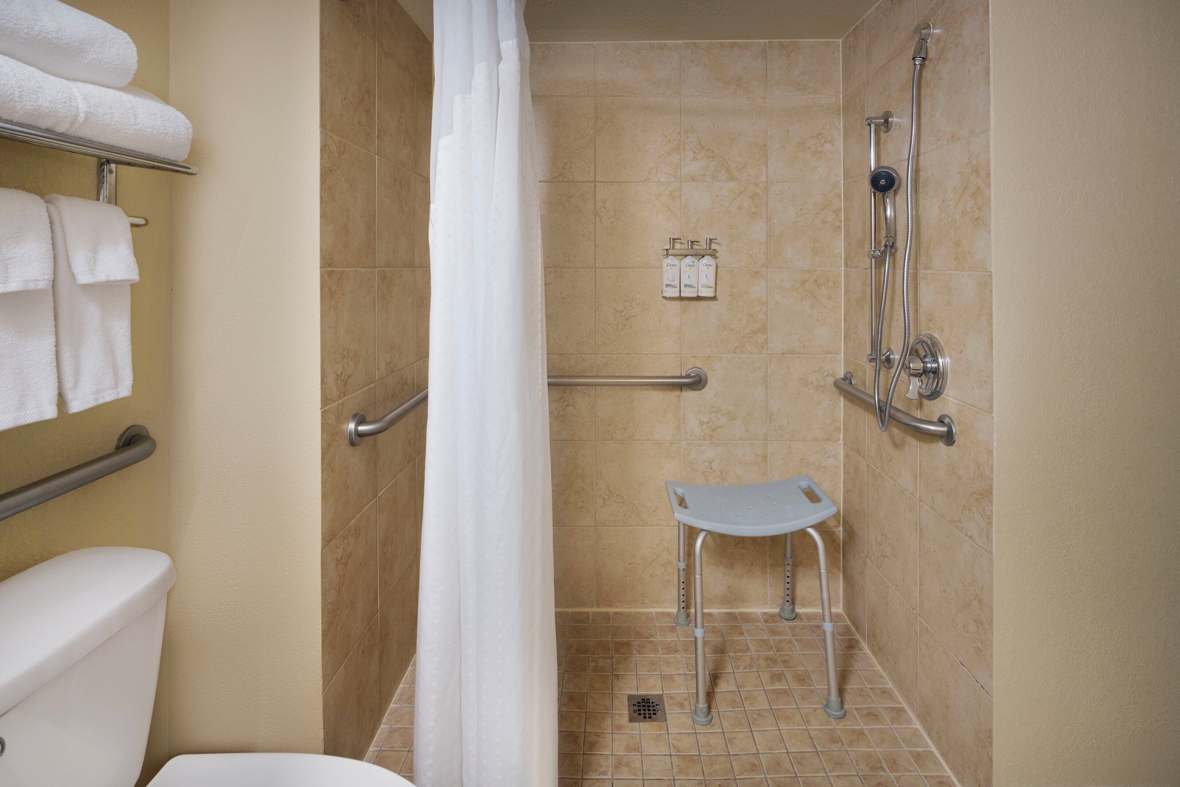 Baño con ducha, inodoro y barra de apoyo.