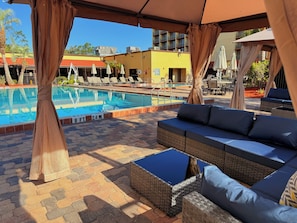 A poolside area with a lounge chair, a small table, and a covered seating area.