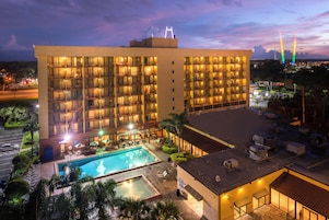 A hotel with multiple floors, a rooftop pool, and a view of the city skyline at dusk.