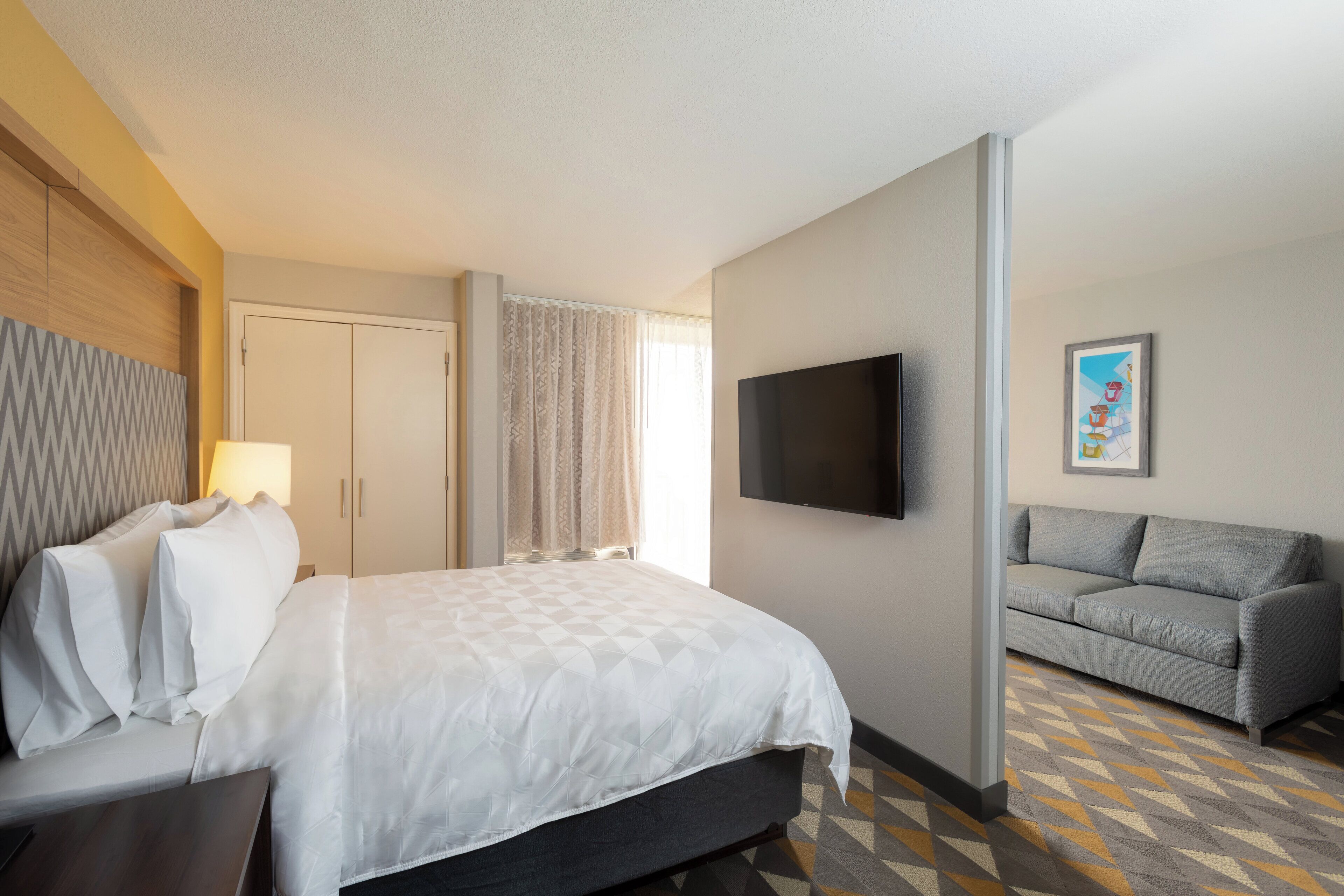 A hotel room with a bed, a sofa, a TV, and a painting on the wall.
