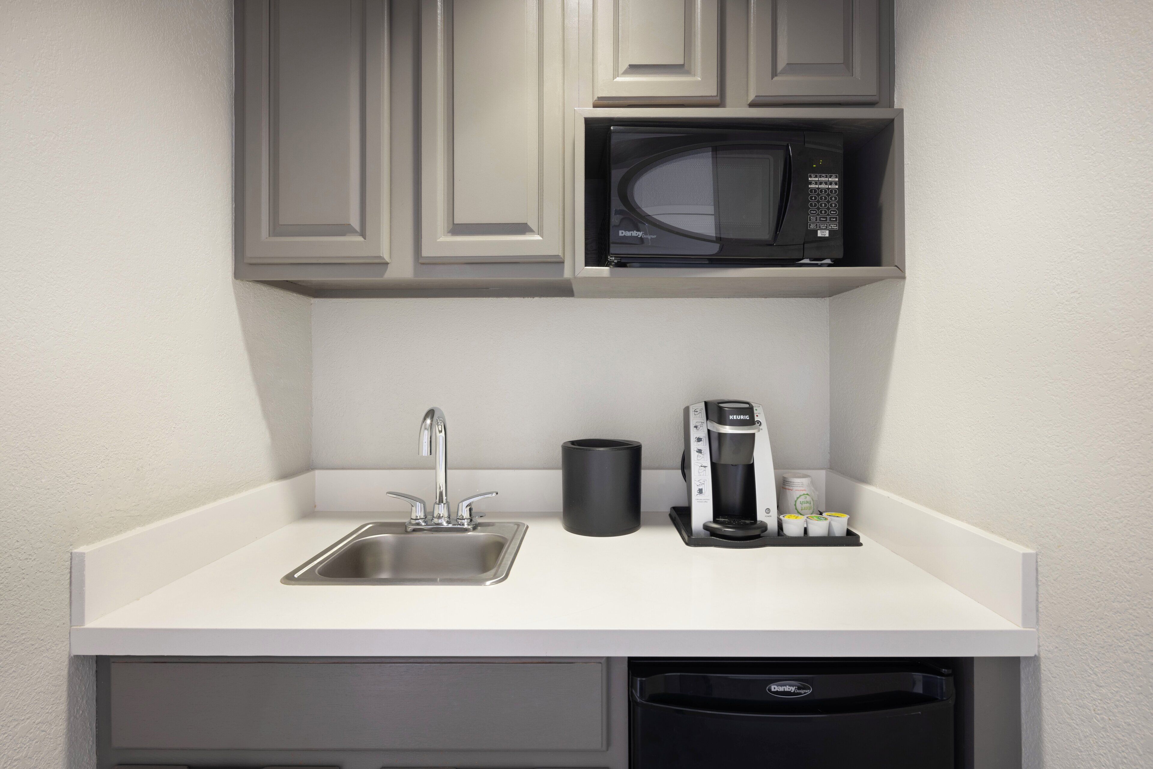 Cocina compacta con lavamanos, microondas, cafetera y basurero.