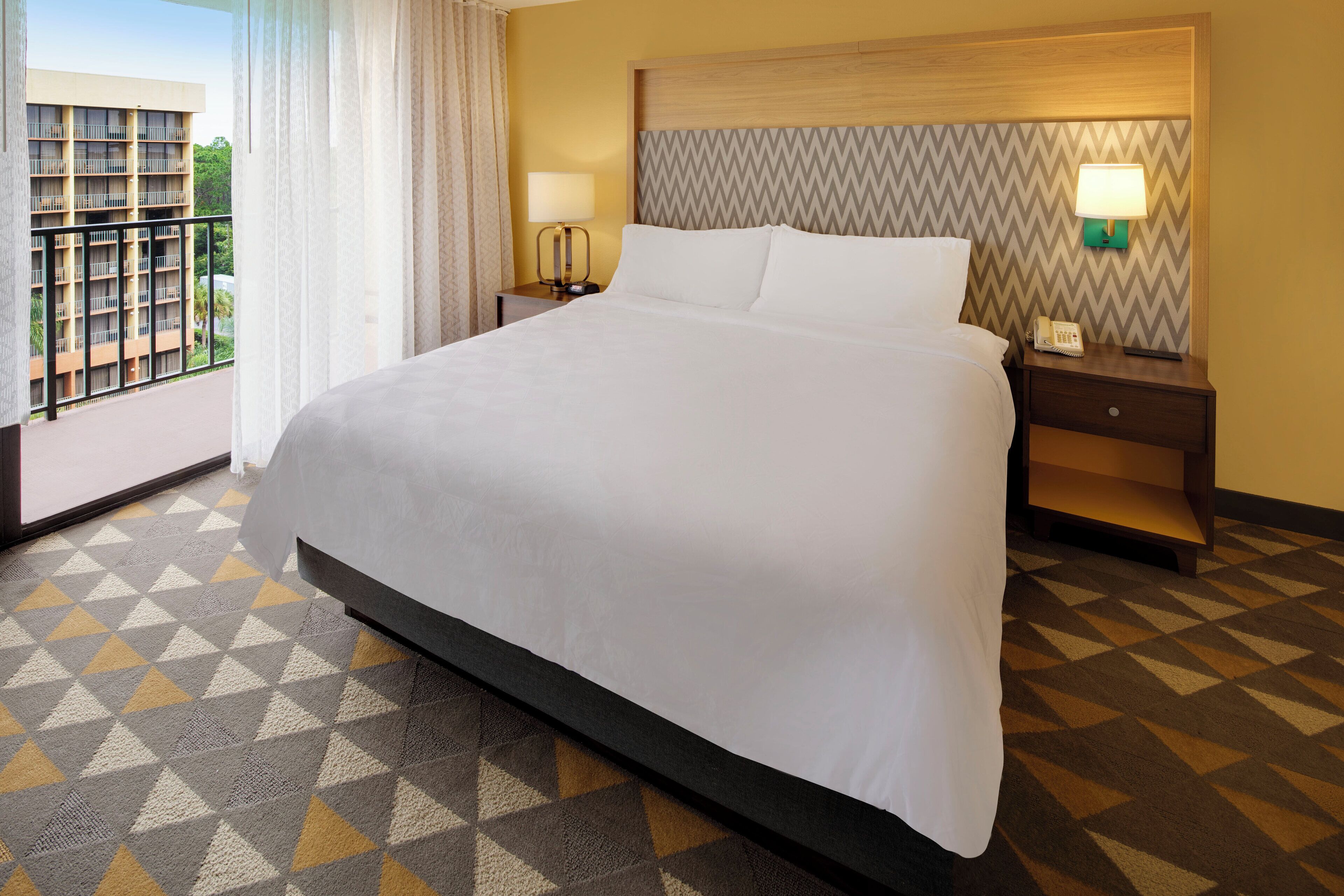 Une chambre d’hôtel avec un grand lit, une table de chevet avec une lampe et une vue sur un immeuble par la fenêtre.