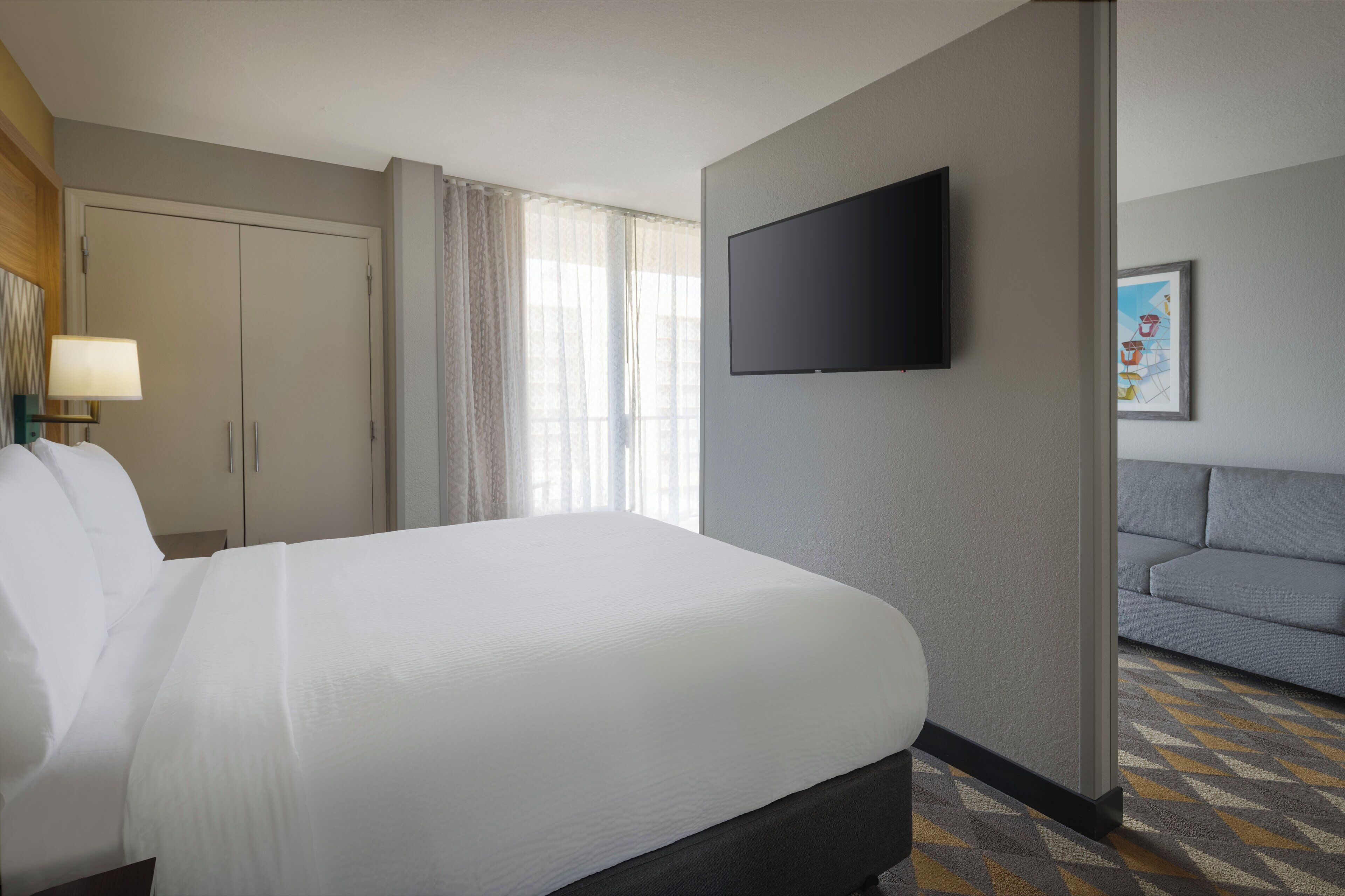 A hotel room with a large bed, a television mounted on the wall, a sofa, and a patterned carpet.