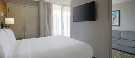 Quarto de hotel com cama grande, televisão na parede, sofá e carpete estampado.