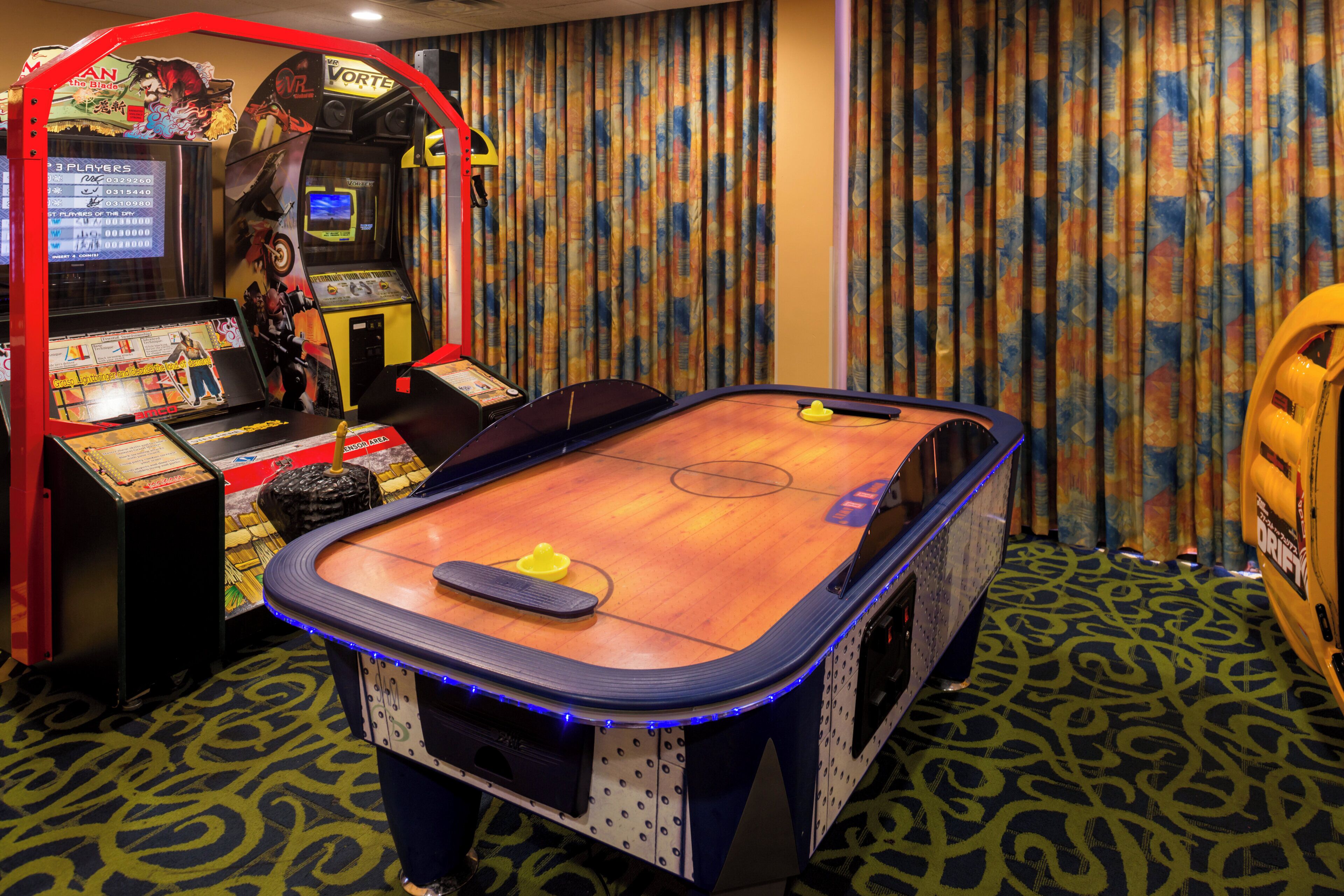 A pool table with a VR gaming station and a dartboard in a room with patterned carpet.
