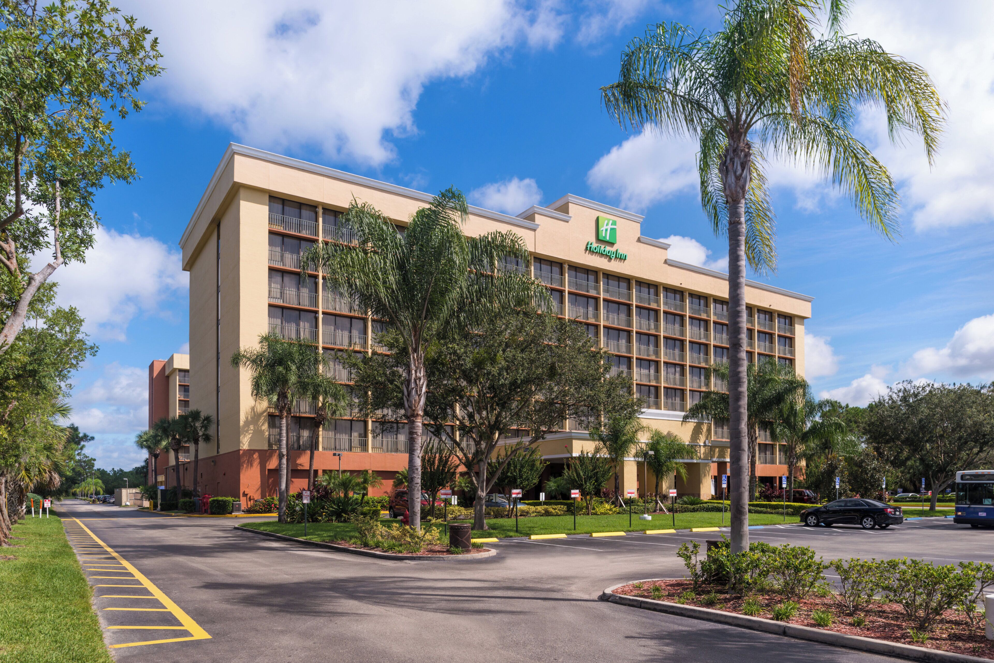A Holiday Inn hotel with a modern design, featuring a large building with multiple floors, a well-maintained lawn, and a parking area.