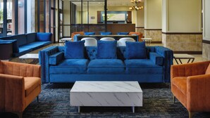 Un hall d’entrée avec un canapé bleu, des fauteuils orange et une table basse en marbre.