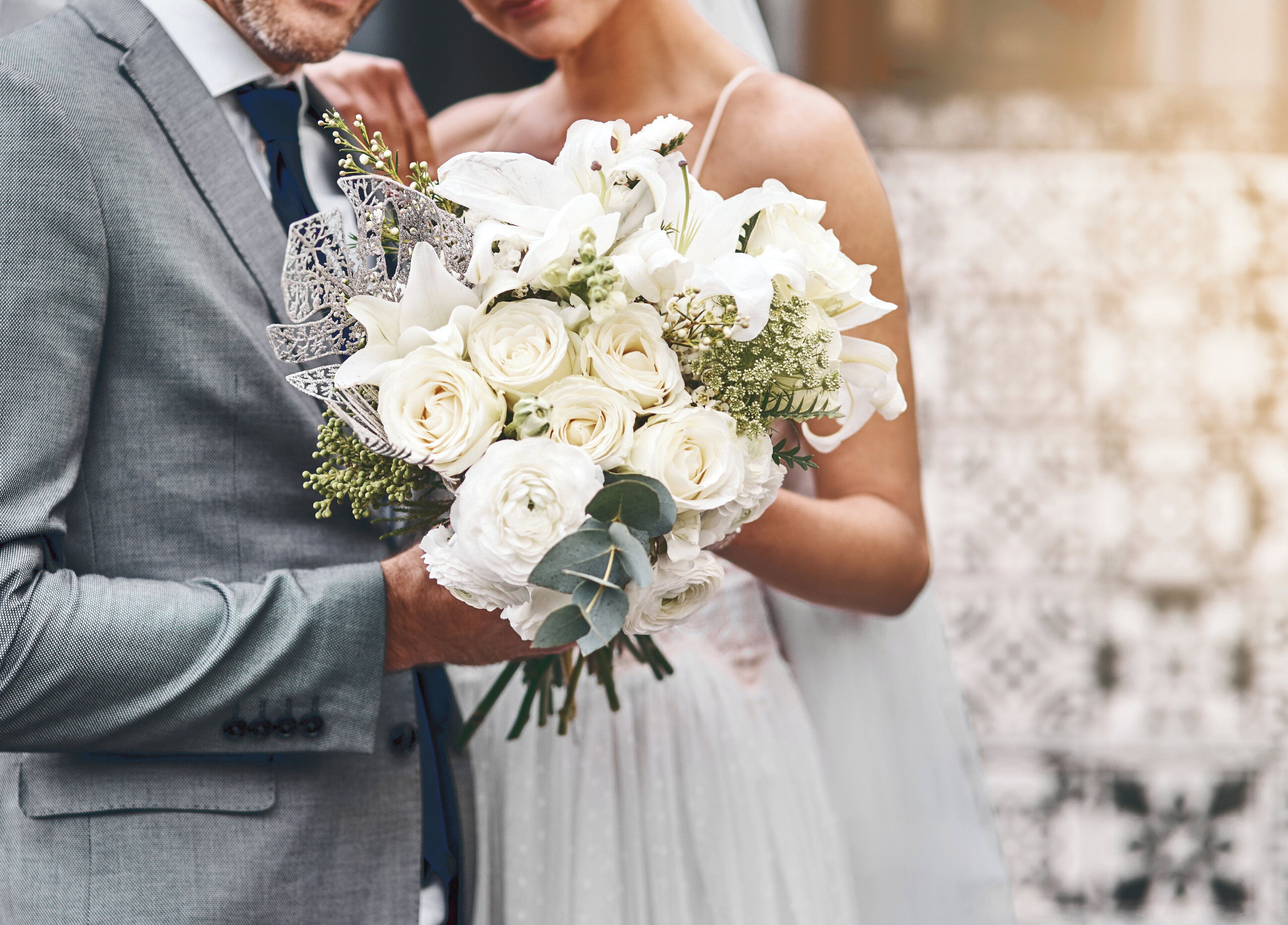 A couple holding a bouquet of white flowers.