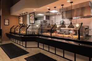 Angolo buffet con separè in vetro, diversi cibi e illuminazione a soffitto.