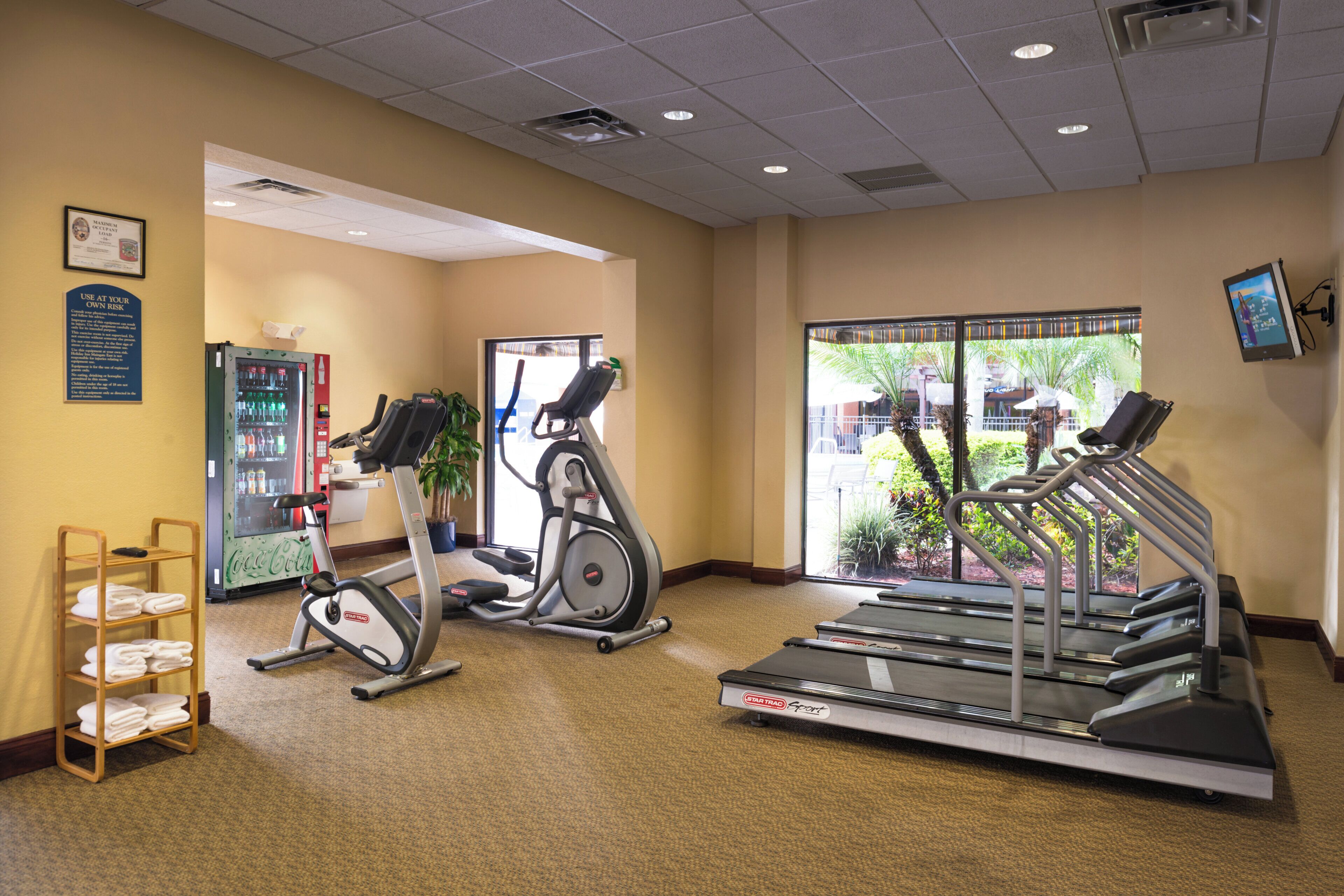 A gym with treadmills, an elliptical, and a Coca-Cola refrigerator.