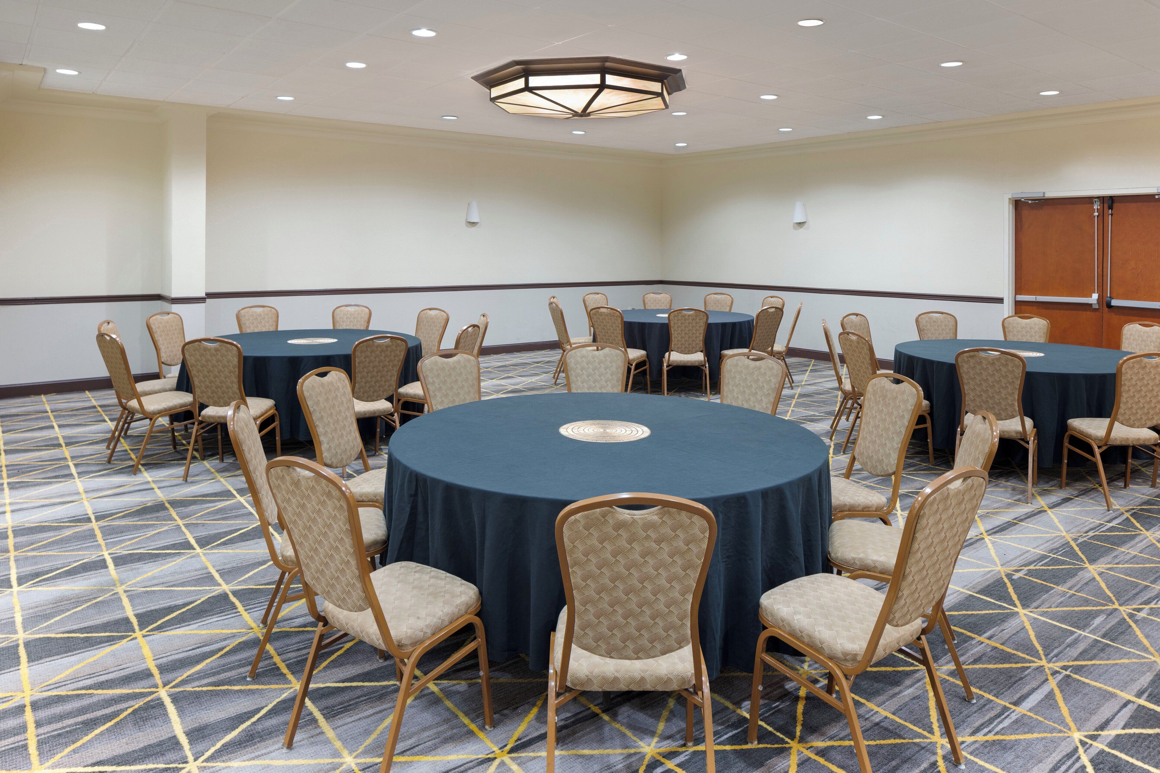 A conference room with round tables and chairs, carpeted floor, and a ceiling light fixture.
