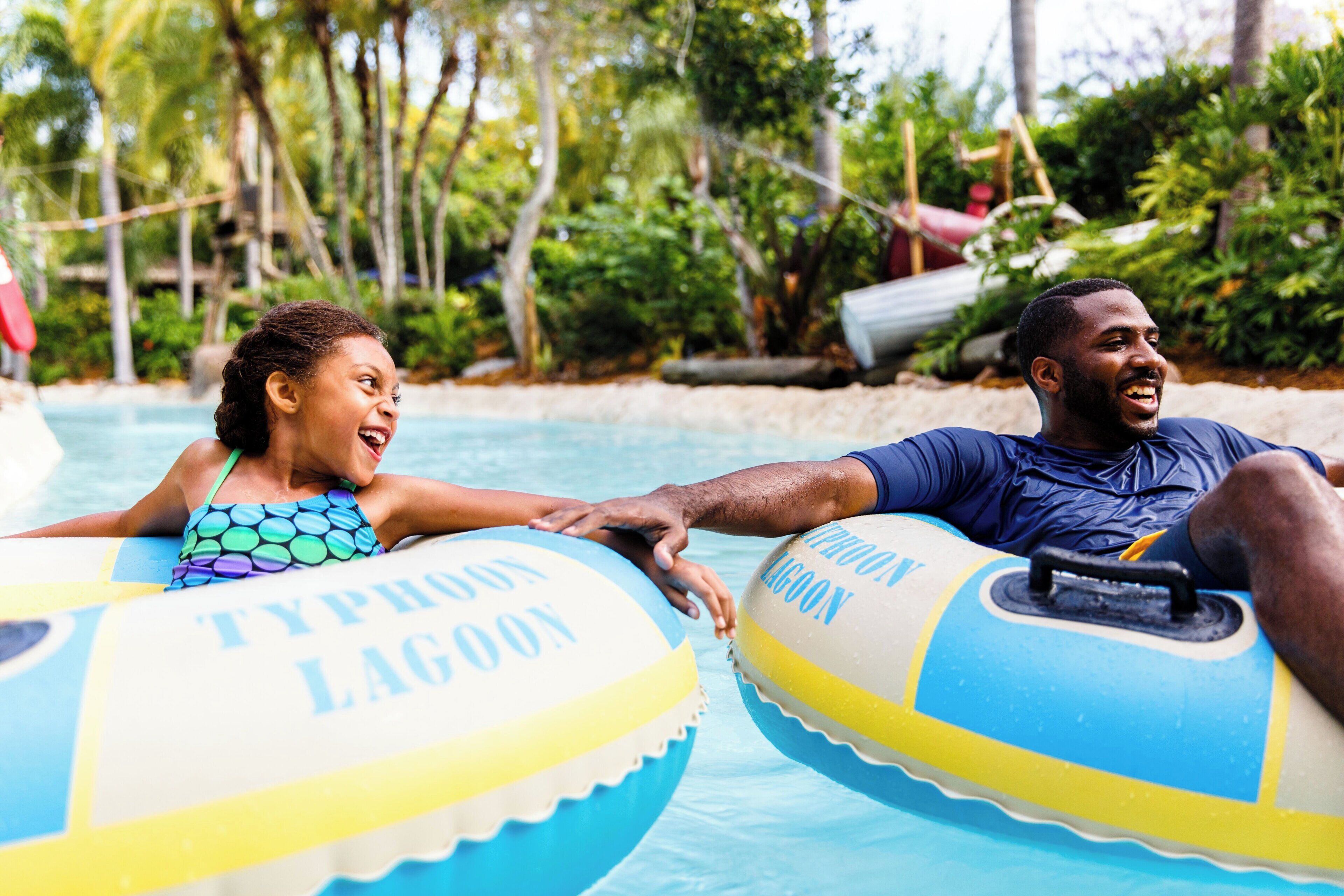 Two people on inflatable tubes in a pool with tropical vegetation in the background.