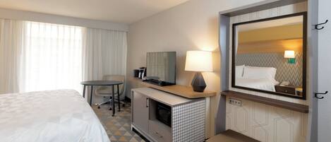Una habitación de hotel con una cama, un escritorio, un televisor, una lámpara y un espejo.