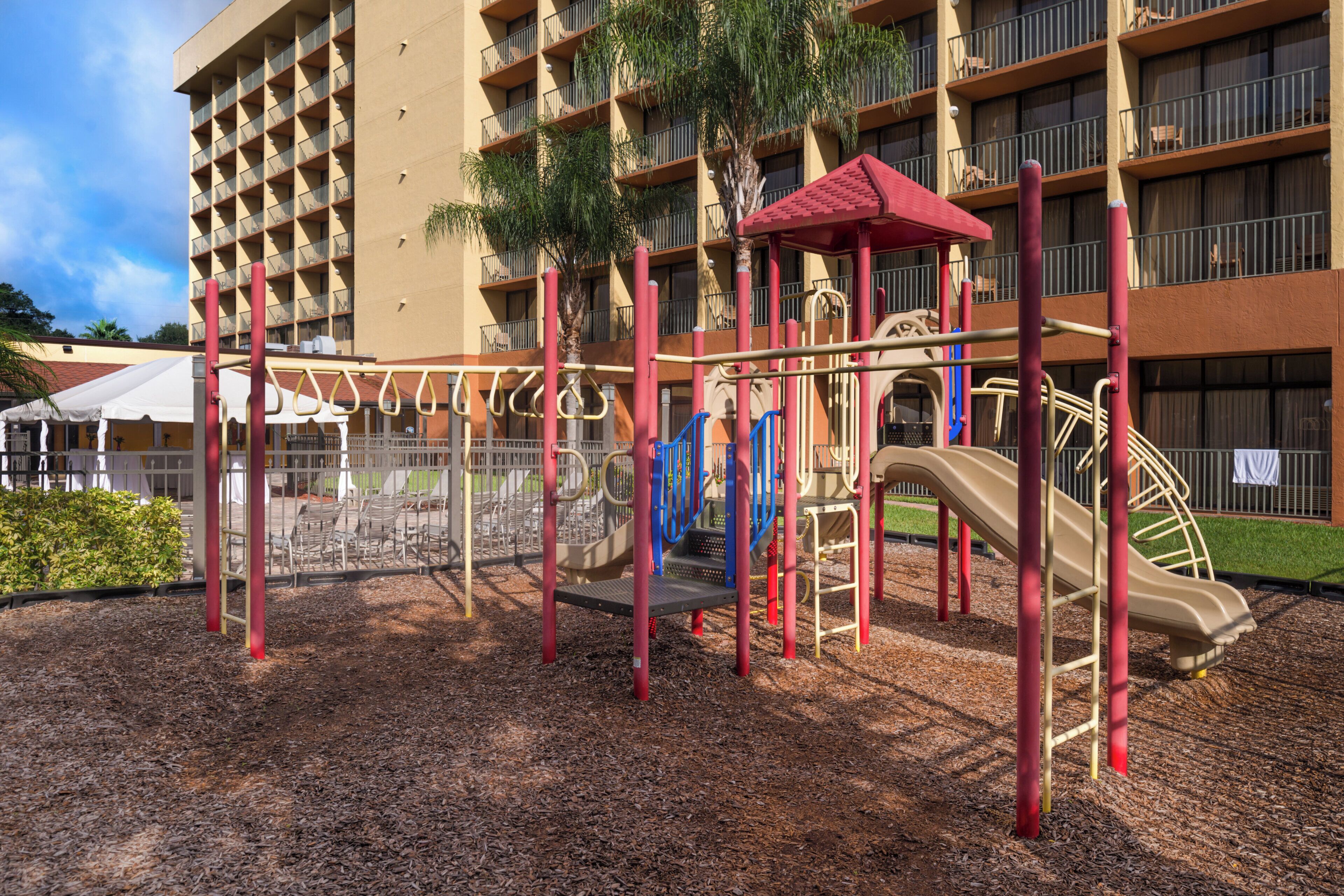 A playground with a slide and climbing structures, surrounded by a building with balconies.
