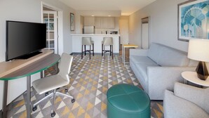 Une chambre d’hôtel moderne équipée d’une télévision à écran plat, d’un bureau, d’un canapé confortable, d’une petite table et d’un coin cuisine avec un tabouret de bar.