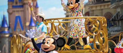 A parade float with Mickey and Minnie Mouse characters, a golden railing, and a backdrop of a castle-like structure.