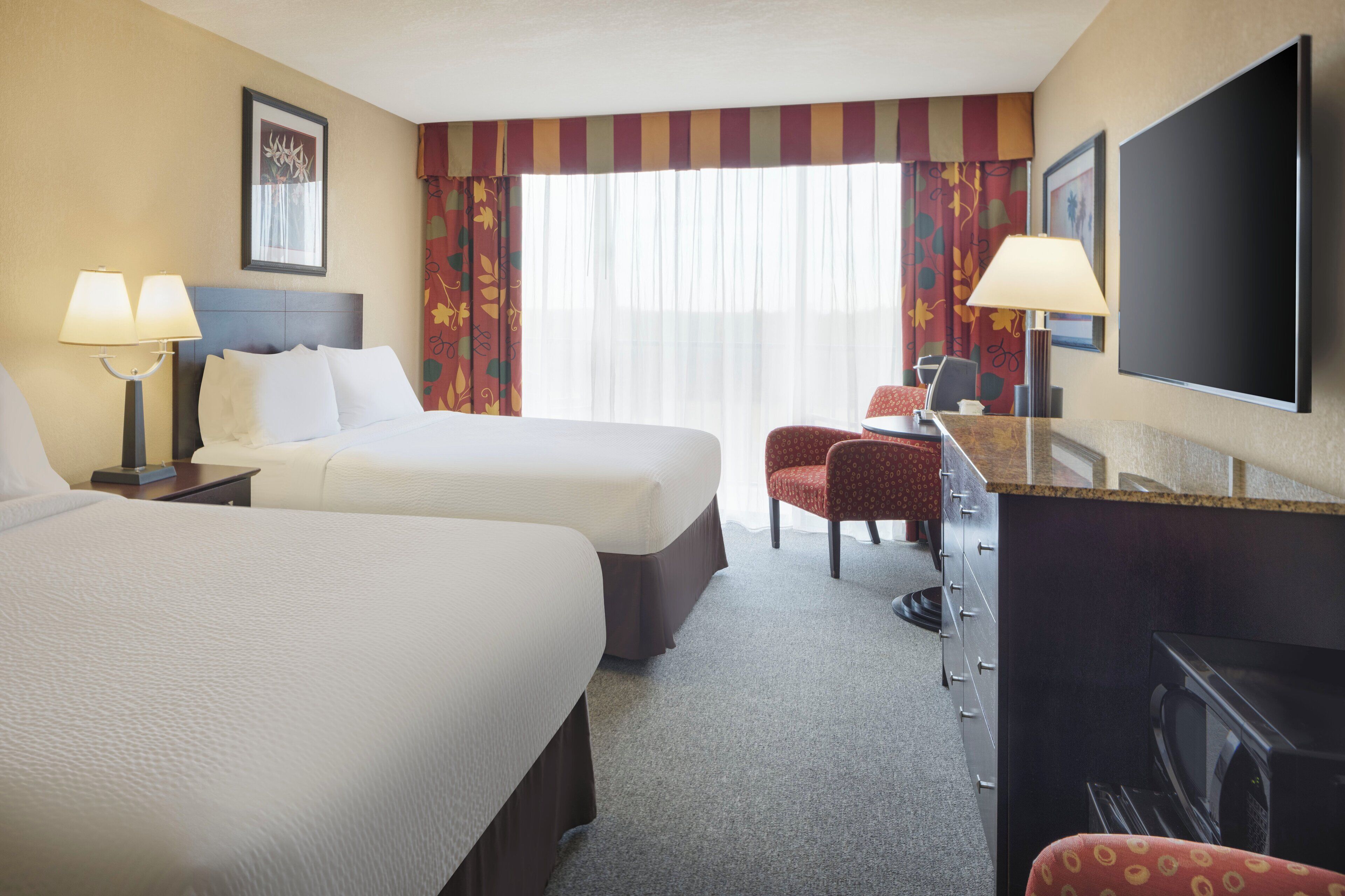 A hotel room with two beds, a desk with a chair, a flat-screen TV, and a fireplace.
