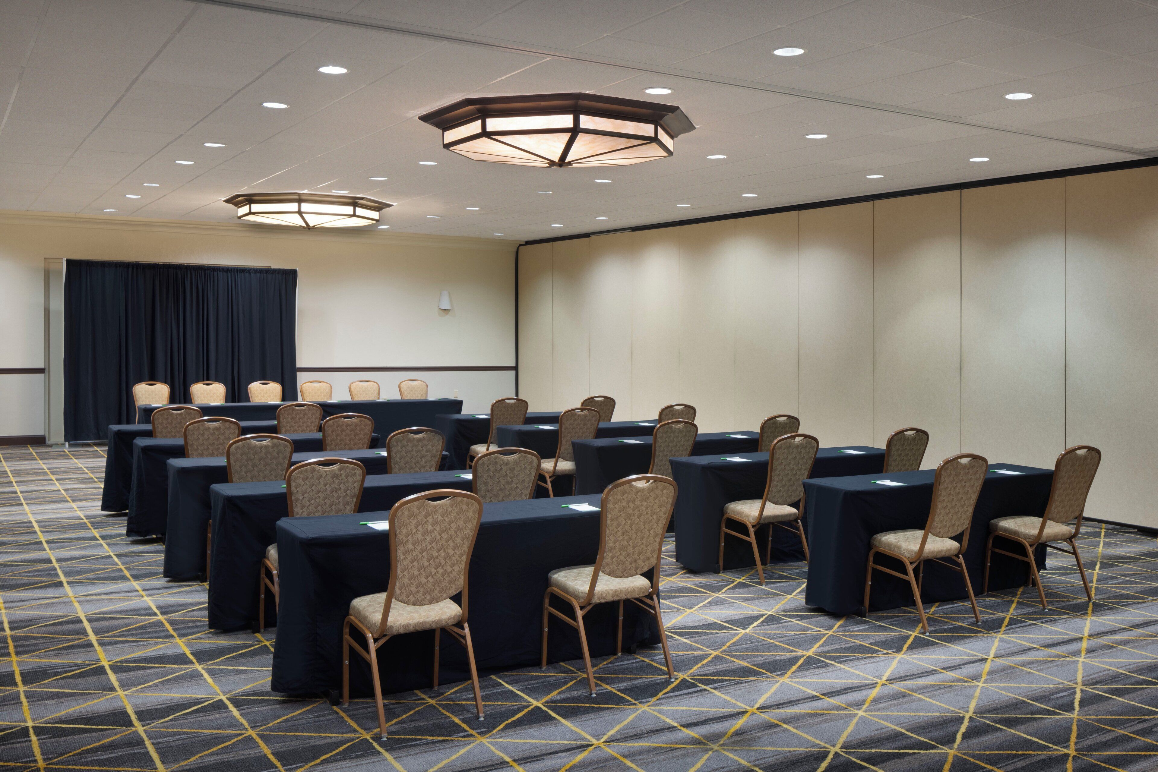 Une salle de conférence équipée de tables et de chaises, recouverte d’un tapis à motifs et dotée d’un plafond avec des luminaires encastrés.