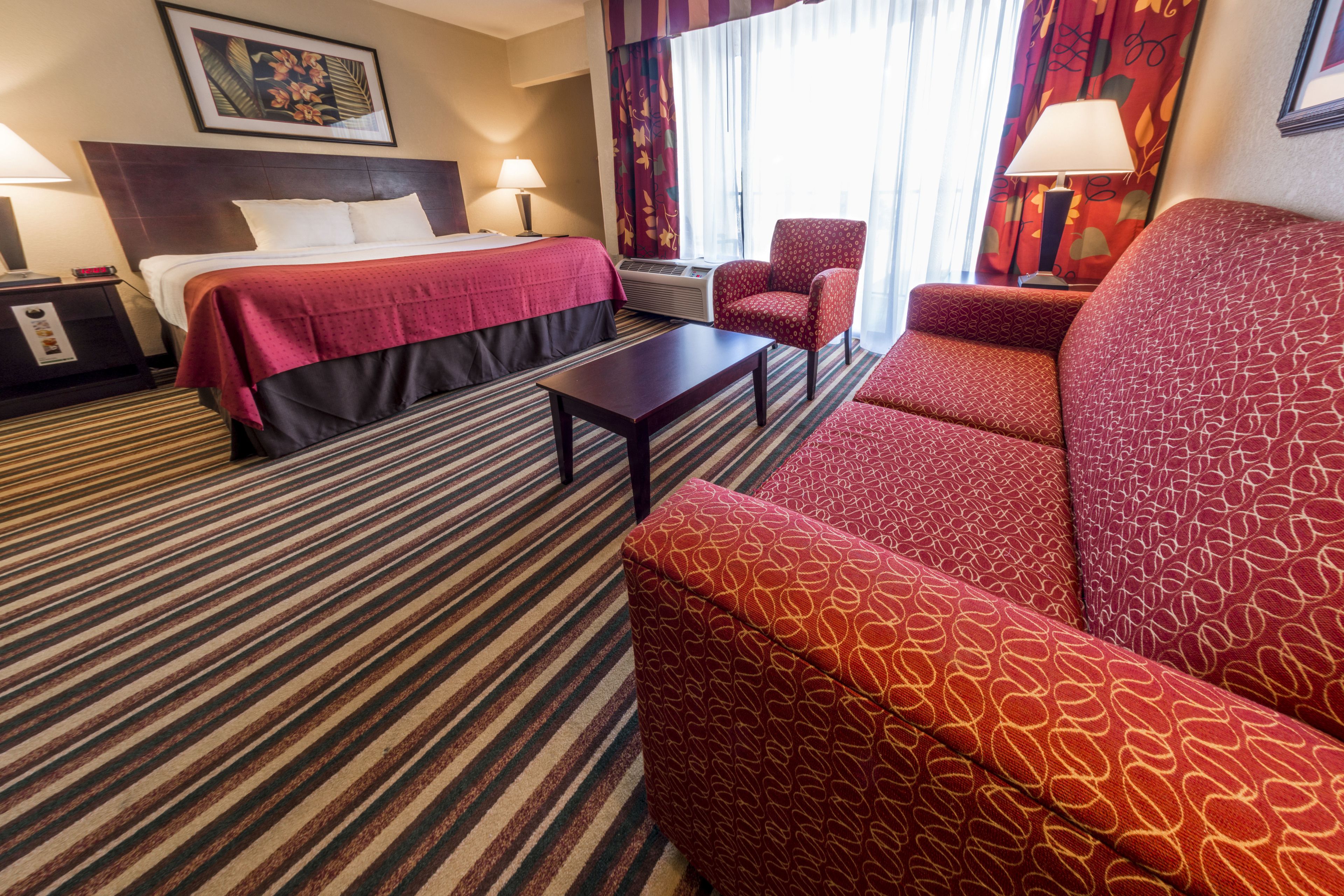 Una habitación de hotel con cama, sofá, sillón, mesa y aire acondicionado.