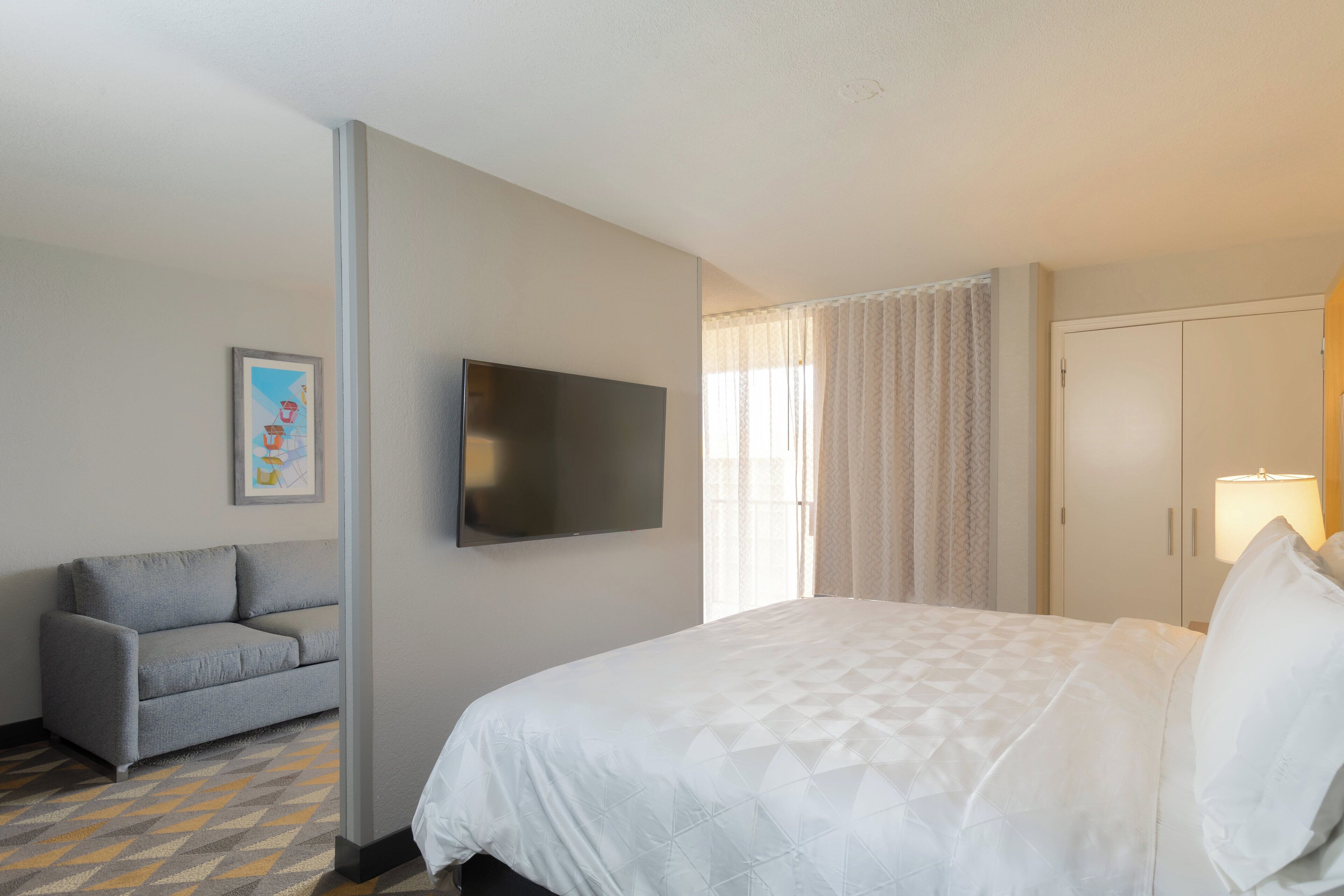 A hotel room with a bed, a sofa, a TV, and a painting on the wall.
