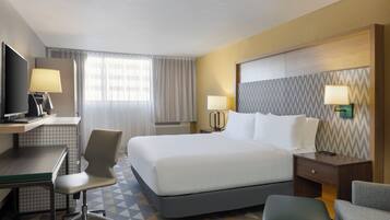 A hotel room with a bed, desk, chair, and TV.