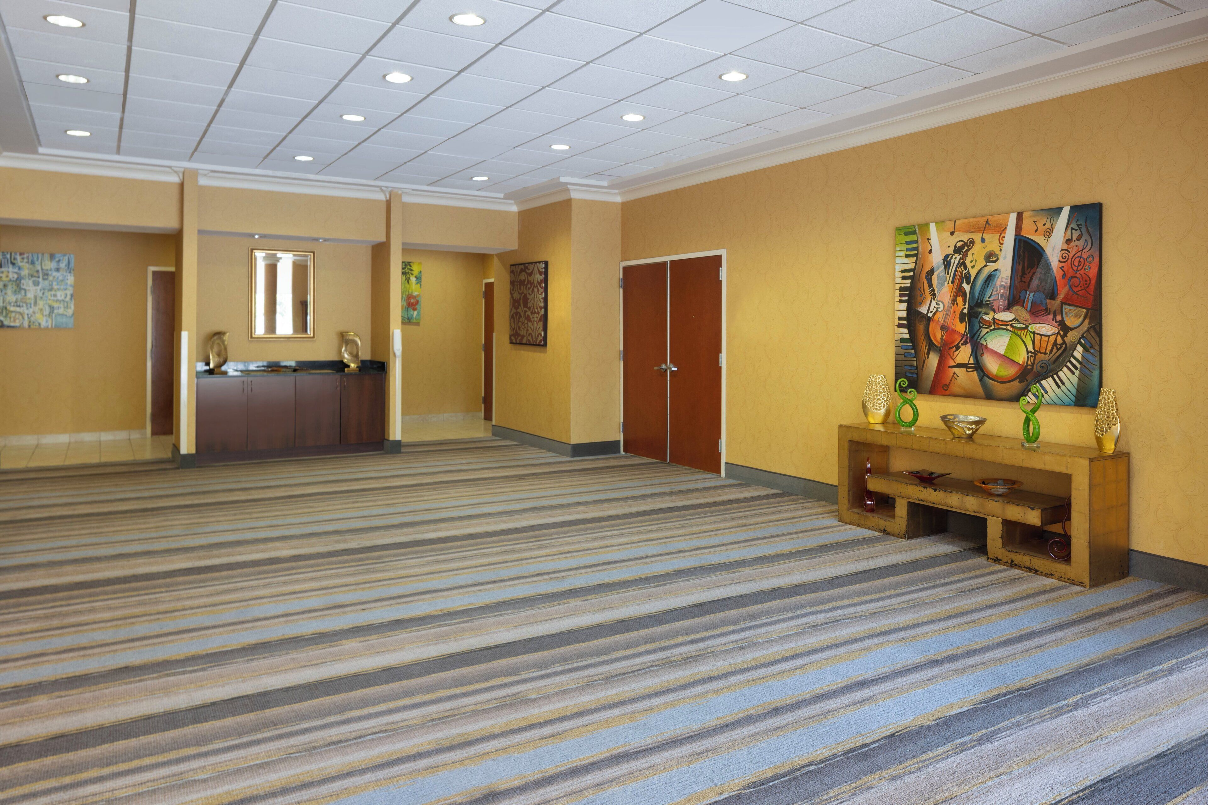 Un pasillo amplio con alfombra a rayas, un mostrador de recepción y un cuadro de colores en la pared.