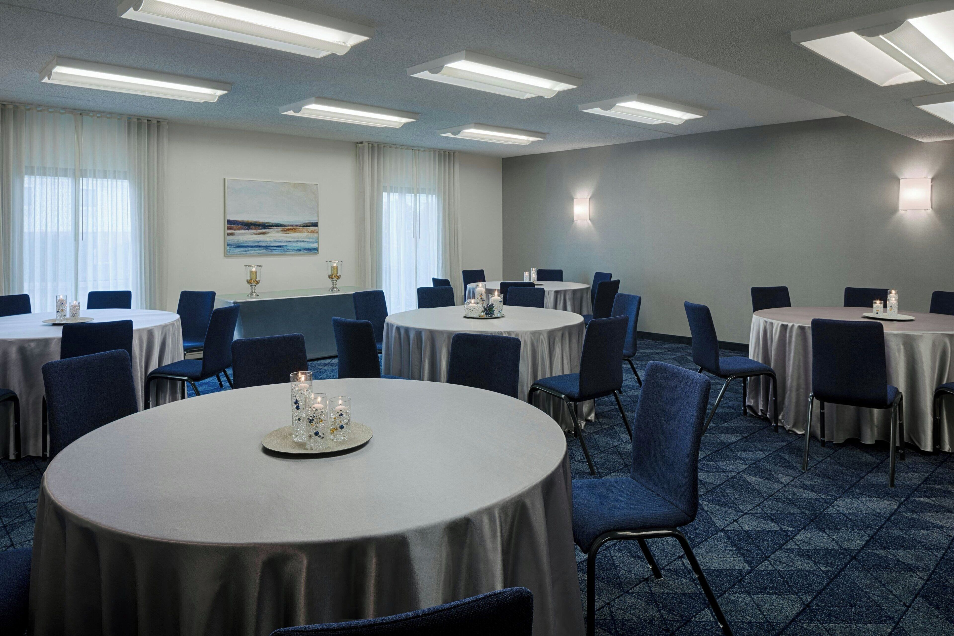 Un salón de conferencias con varias mesas redondas, cada una rodeada de sillas, y un cuadro grande en la pared.
