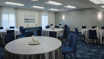 Un salón de conferencias con varias mesas redondas, cada una rodeada de sillas, y un cuadro grande en la pared.