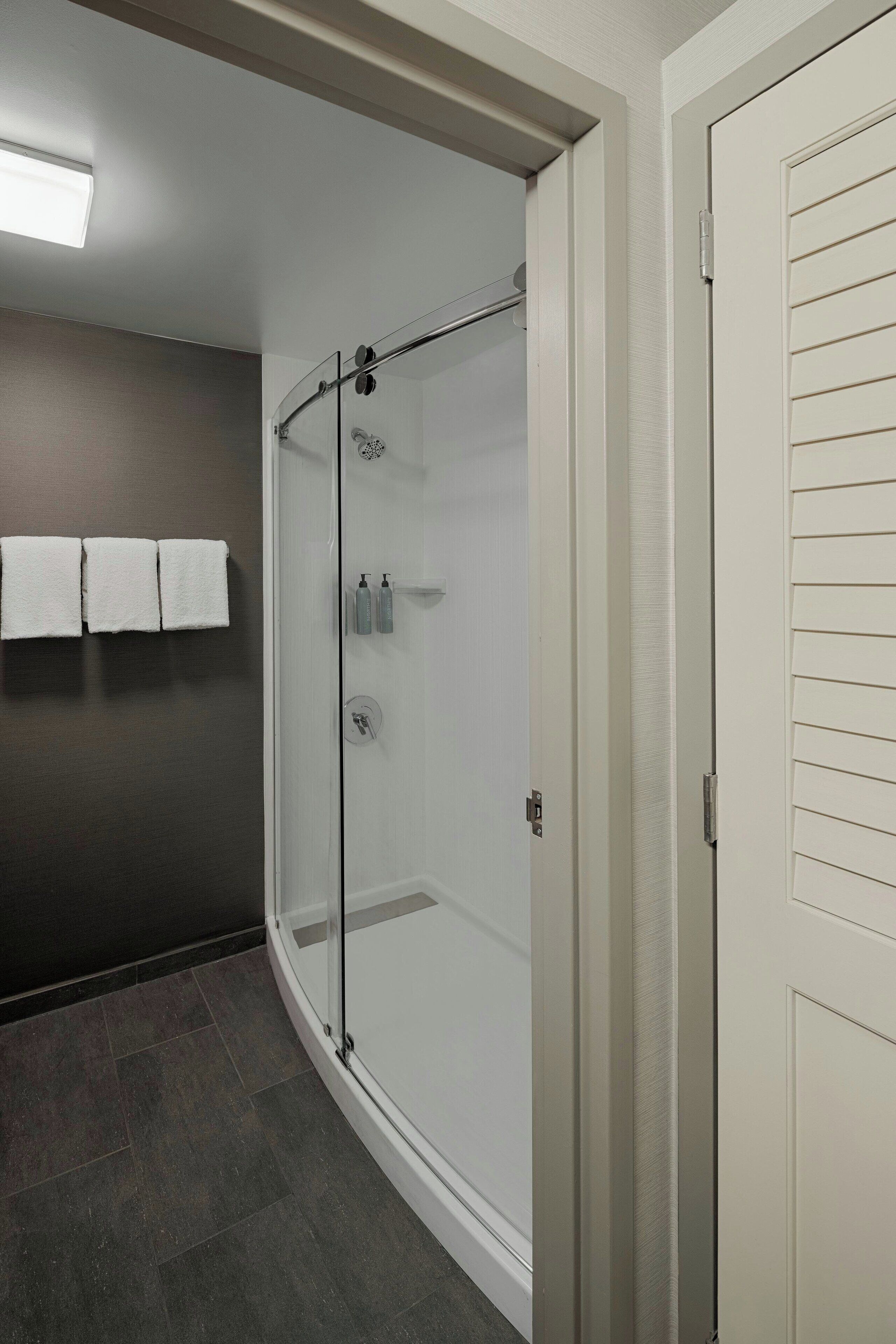 Un baño moderno con ducha de mampara de vidrio, pisos de baldosas oscuras y una puerta blanca.