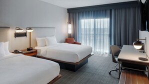 A hotel room with two beds, a desk, a chair, and a large window with curtains.