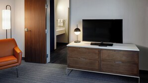 A hotel room with a wooden door, a TV on a white console, a modern lamp, and a patterned rug.