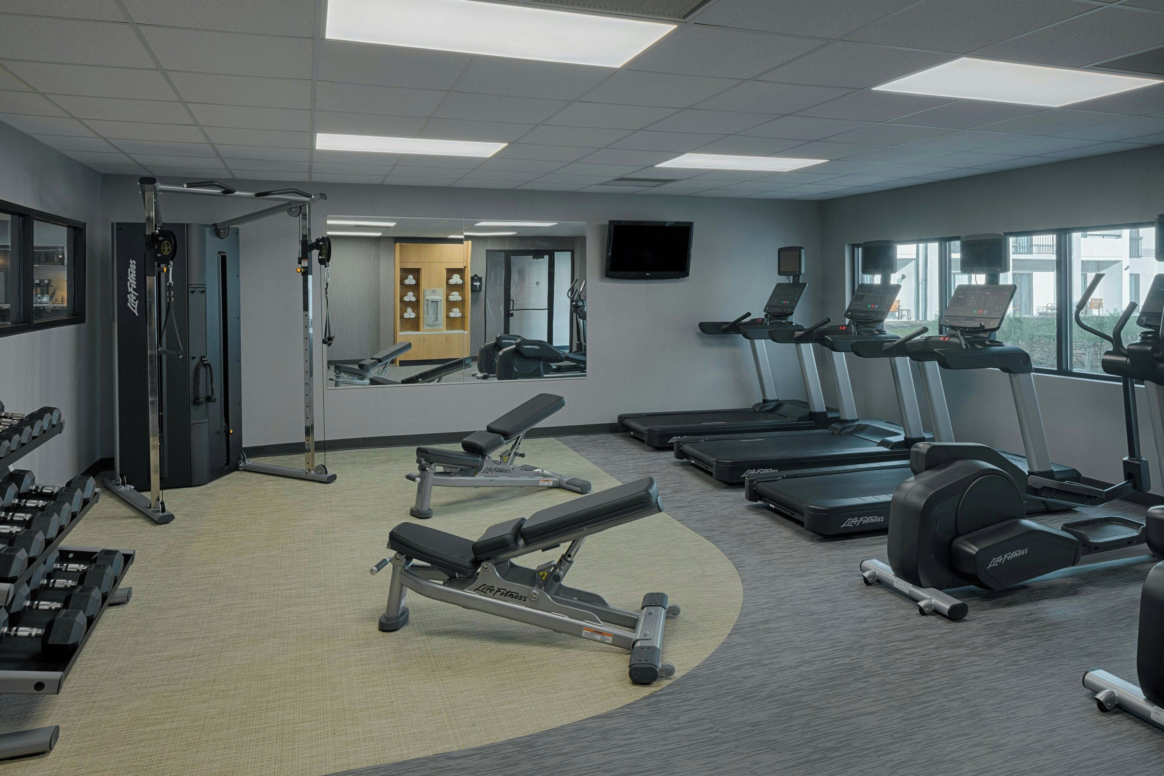 Une salle de sport équipée de tapis de course, d’appareils de musculation et d’haltères.