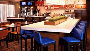 A modern bar area with multiple seating options, a central bar counter, and a variety of beverages and snacks displayed on shelves.